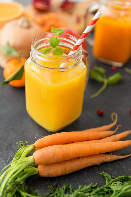 food , healthy eating and vegetarian concept - mason jar glasses of orange juice with paper straw and carrots on slate table