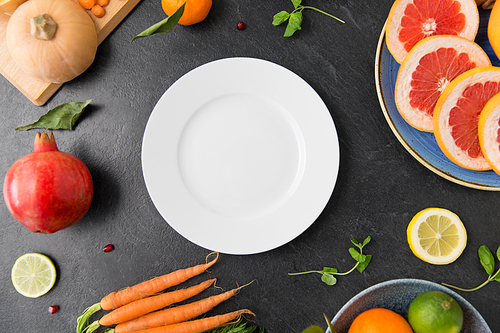 healthy eating, vegetarian food, diet and culinary concept - empty white plate and different vegetables and fruits on on slate table