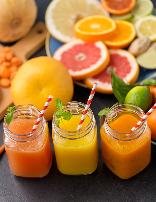 food , healthy eating and vegetarian concept - mason jar glasses of orange and carrot juices with paper straws, fruits and vegetables on slate table