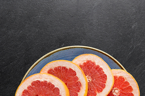 food, fruits and healthy eating concept - close up of fresh juicy sliced grapefruits on plate on slate background