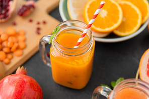 food , healthy eating and vegetarian concept - mason jar glass of orange or carrot juice with paper straw and citrus fruits on slate table top