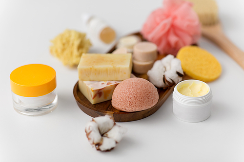 beauty, spa and wellness concept - close up of konjac sponge, crafted soap bars, body butter and cream on wooden tray