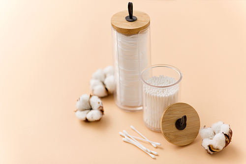 beauty and hygiene concept - close up of cotton pads and swabs in holders on beige background
