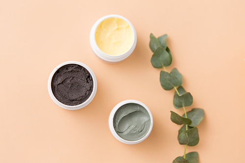 beauty, spa and wellness concept - blue clay mask, body butter, therapeutic mud and eucalyptus cinerea on beige background