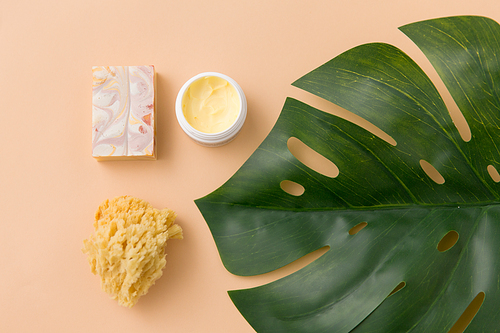 beauty, spa and bath concept - close up of crafted soap bar, natural sponge with body butter and monstera deliciosa leaf on beige background