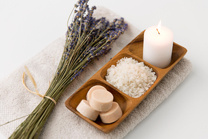 beauty and wellness concept - sea salt, soap and candle on wooden tray and bunch of lavender on bath towel