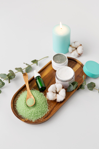 beauty and spa concept - green bath salt, serum with dropper, moisturizer, blue clay mask and eucalyptus cinerea with cotton flowers on wooden tray