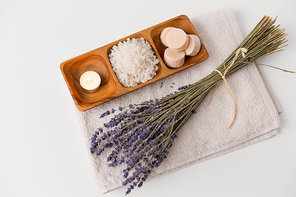 beauty and wellness concept - sea salt, soap and tea candle on wooden tray and bunch of lavender on bath towel