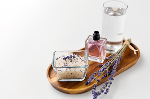 beauty and wellness concept - sea salt, perfume, lavender and glass of water on wooden tray