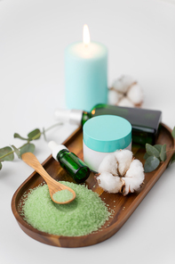 beauty and spa concept - green bath salt, serum with dropper or essential oil, moisturizer and eucalyptus cinerea with cotton flowers on wooden tray