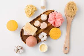 beauty, spa and wellness concept - close up of konjac sponge, crafted soap bars on wooden tray and body butter with natural bristle brush