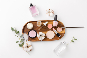 beauty, natural cosmetics and make up products concept - makeup, perfume with cotton flower on wooden tray and eucalyptus cinerea