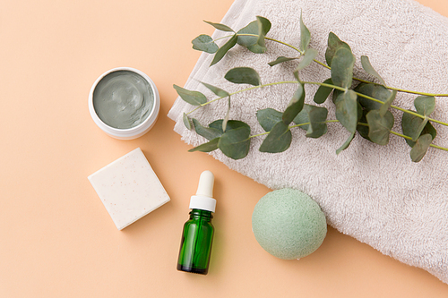 beauty and spa concept - serum or essential oil, clay mask, soap bar, konjac sponge and eucalyptus cinerea on bath towel