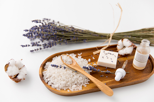 beauty and wellness concept - 씨솔트 with spoon, soap, serum with dropper, lavender and cotton flowers on wooden tray