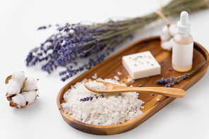 beauty and wellness concept - sea salt with spoon, soap, serum with dropper, lavender and cotton flowers on wooden tray
