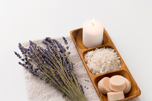beauty and wellness concept - sea salt, soap and candle on wooden tray and bunch of lavender on bath towel