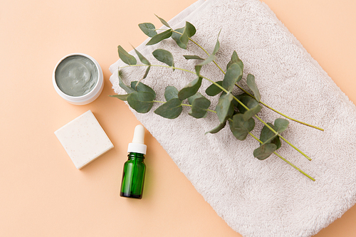 beauty, spa and wellness concept - serum or essential oil, clay mask, soap bar and eucalyptus cinerea on bath towel