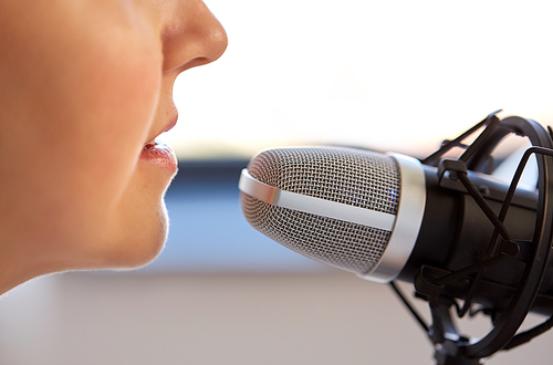 technology, mass media and people concept - close up of woman with microphone talking and recording podcast at studio