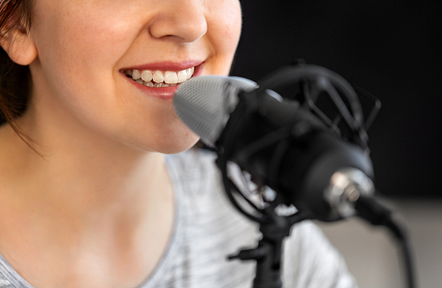 technology, mass media and people concept - close up of woman with microphone talking and recording podcast at studio