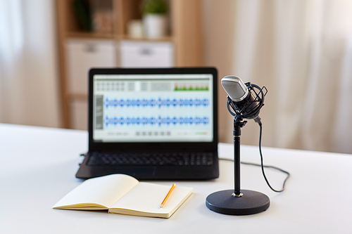 post production and technology concept - microphone, laptop computer with sound editor program, headphones and notebook on table at home office