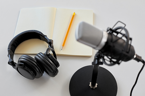 technology, sound recording and podcast concept - headphones , microphone and notebook with pencil on white background