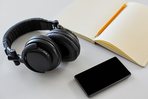 technology and objects concept - headphones, smartphone and notebook with pencil on white background