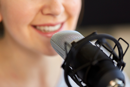 technology, mass media and people concept - close up of woman with microphone talking and recording podcast at studio