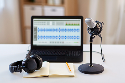 post production and technology concept - microphone, laptop computer with sound editor program, headphones and notebook on table at home office