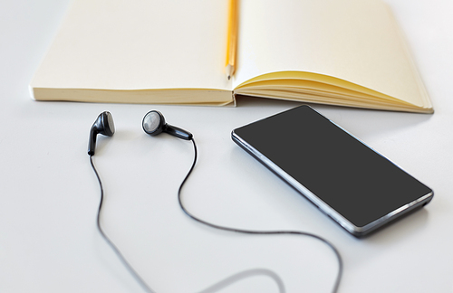 technology and objects concept - earphones, smartphone and notebook with pencil on white background