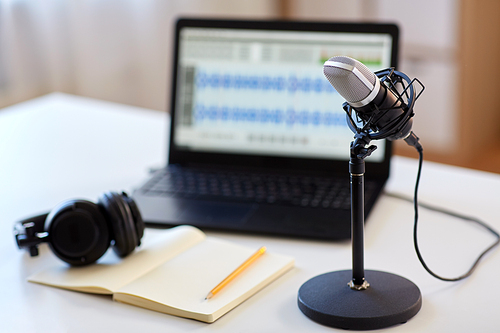 post production and technology concept - microphone, laptop computer with sound editor program, headphones and notebook on table at home office