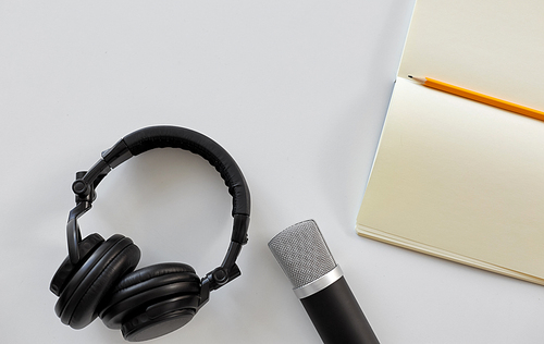 technology, sound recording and podcast concept - headphones , microphone and notebook with pencil on white background