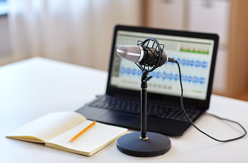 post production and technology concept - microphone, laptop computer with sound editor program, headphones and notebook on table at home office