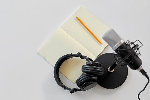 technology, sound recording and podcast concept - headphones , microphone and notebook with pencil on white background