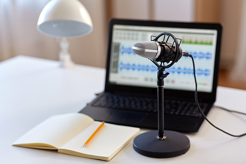 post production and technology concept - microphone, laptop computer with sound editor program, headphones and notebook on table at home office