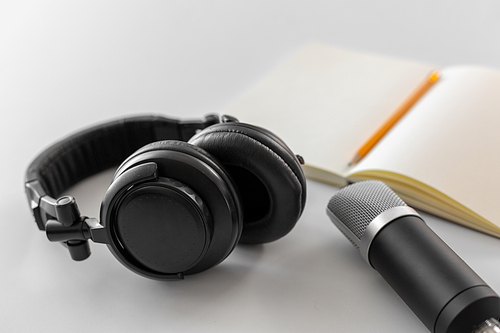 technology, sound recording and podcast concept - headphones , microphone and notebook with pencil on white background