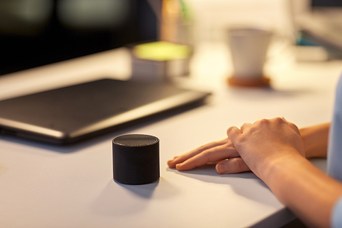 technology and people concept - close up of hand with smart speaker on table at night office