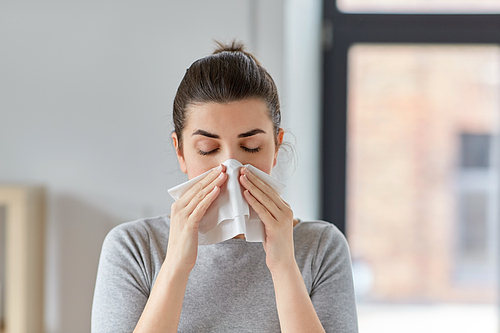 healthcare, cold, allergy and people concept - sick woman blowing her runny nose in paper tissue at home