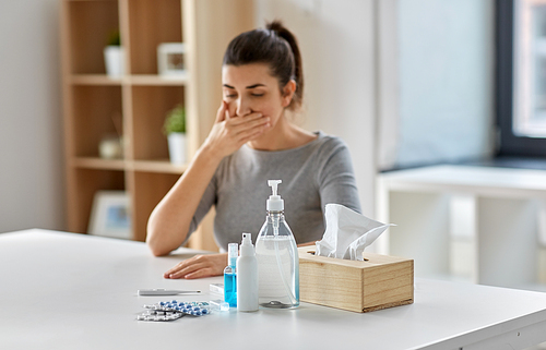 people, health and fever concept - medicines and sanitizers on table over sick woman coughing at home