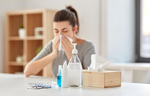 health care, virus and people concept - medicines and sanitizers on table over sick woman blowing nose to paper wipe at home