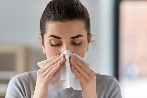 healthcare, cold, allergy and people concept - close up of sick woman blowing her runny nose in paper tissue at home