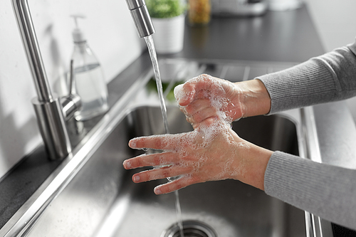 hygiene, health care and safety concept - close up of woman washing hands with liquid soap in kitchen at home