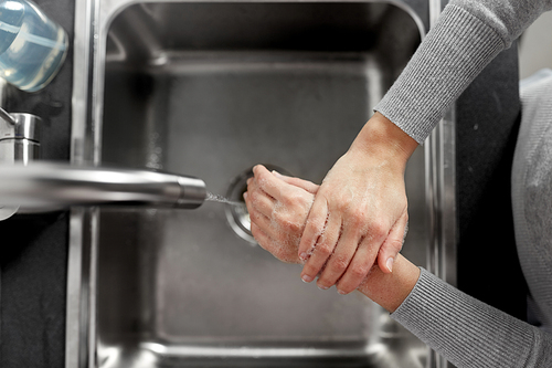 hygiene, health care and safety concept - close up of woman washing hands with liquid soap in kitchen at home