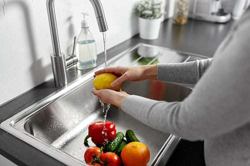 hygiene, health care and safety concept - close up of woman washing fruits and vegetables in kitchen at home