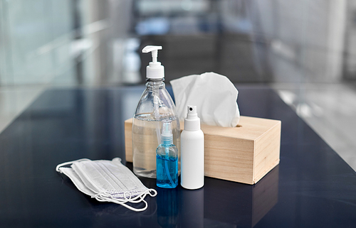 hygiene and disinfection concept - close up of different hand sanitizers, liquid soap, face protective medical masks and paper tissues on table