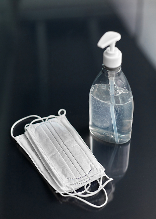 hygiene and disinfection concept - close up of hand sanitizer or liquid soap and face protective medical masks on table