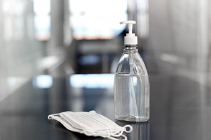 hygiene and disinfection concept - close up of hand sanitizer or liquid soap and face protective medical masks on table