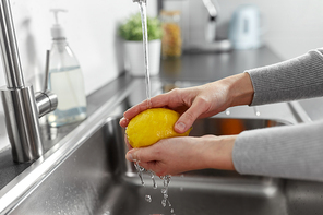 hygiene, health care and safety concept - close up of woman's hands washing lemon fruit in kitchen at home