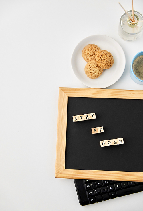 quarantine, epidemic and safety concept - close up of chalkboard with stay at home words on wooden toy blocks, coffee cup, cookies and book with aroma reed diffuser on white background