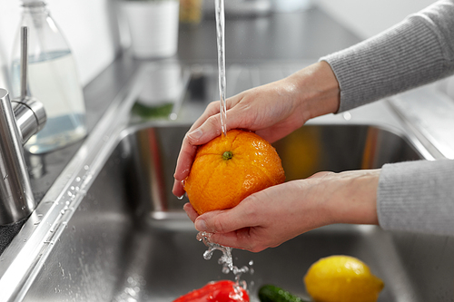 hygiene, health care and safety concept - close up of woman's hands washing fruits and vegetables in kitchen at home