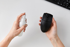 hygiene, cleaning and disinfection concept - close up of woman hands spraying hand sanitizer to computer mouse